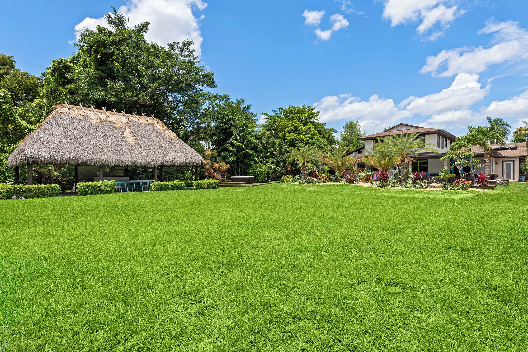 A well-maintained lawn with a thatched-roof structure and a modern house in the background.