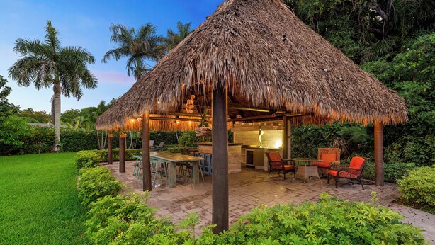 A thatched-roof outdoor dining area with a kitchen, seating, and lush greenery. - Blockchain Manor (North Miami Beach)