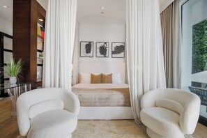 Une chambre à coucher comprenant un lit, deux chaises, une table de chevet, une plante en pot et des œuvres d’art accrochées au mur.