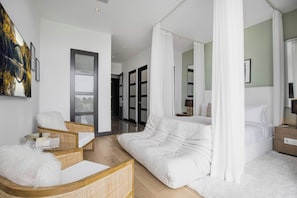 Un dormitorio moderno con una cama grande, un sillón tipo chaise y un baño con paredes de vidrio.