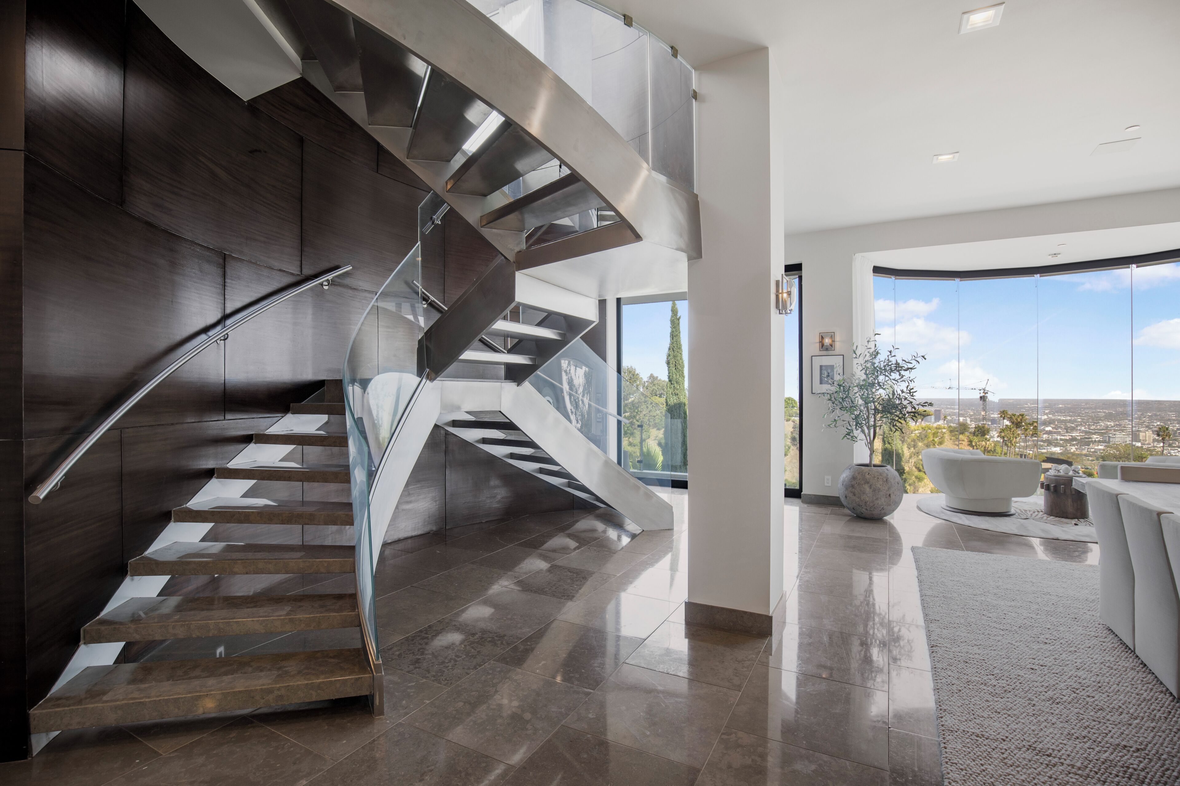 Un interior moderno con una escalera espiral, un ventanal con vista a la ciudad y una zona de estar minimalista.