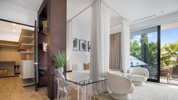 A modern living room with a glass table, clear chairs, a white sofa, and a large window with a view of greenery. - Beverly Crest (Beverly Hills)