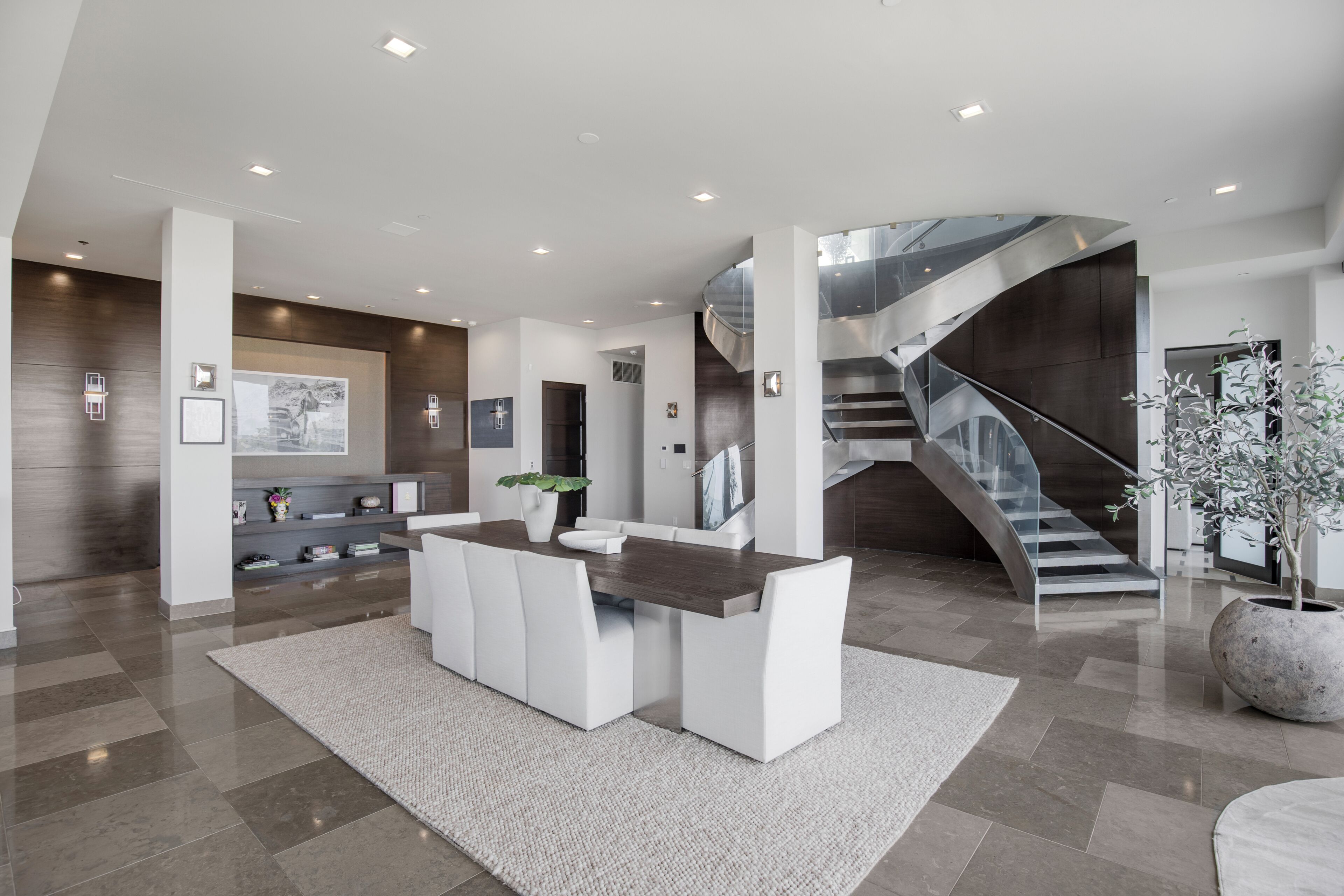 Um interior moderno com uma área de jantar central, uma escada e uma grande planta em vaso.