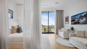A modern living room with a sofa, a bed, and a large window with a view of a building. - Beverly Crest (Beverly Hills)