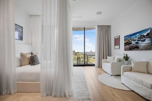 A modern living room with a sofa, a bed, and a large window with a view of a building. - Beverly Crest (Beverly Hills)