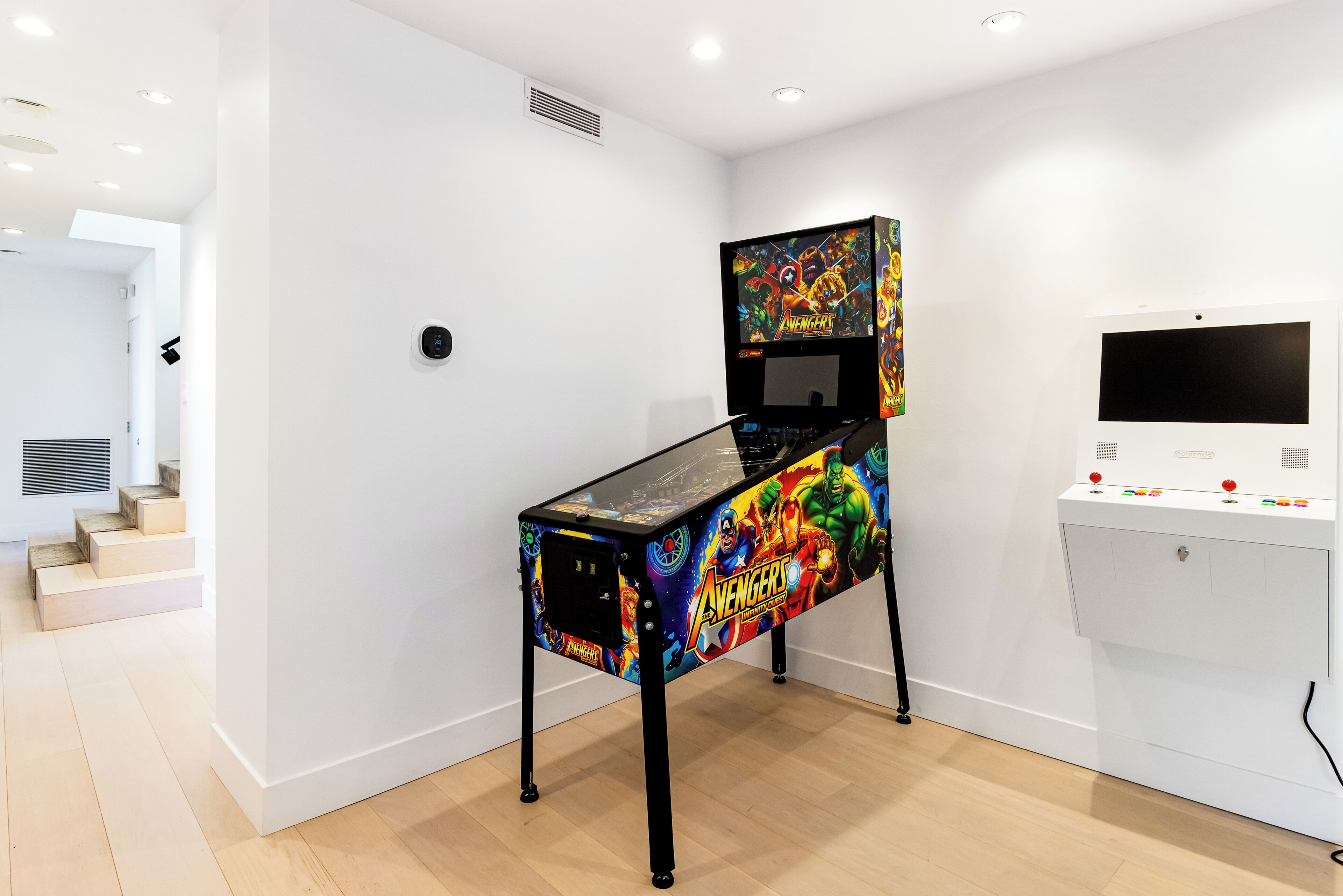 A room with a gaming console table, a white wall, and a staircase.