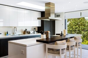 A modern kitchen with a central island, bar stools, and a view of greenery outside. - Saint Ives Reserve (West Hollywood)