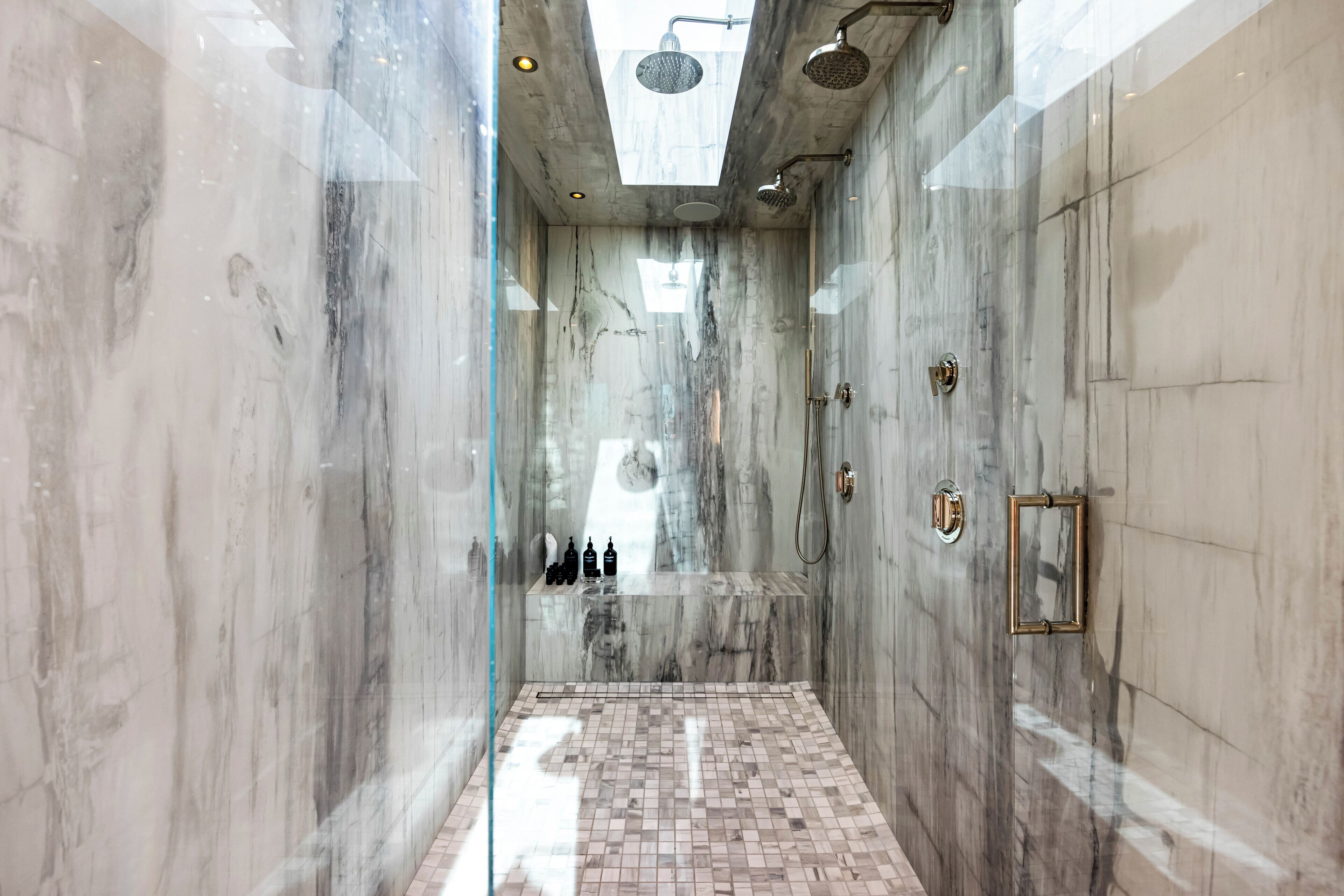A modern bathroom with a glass shower enclosure, marble walls, and a tiled floor.