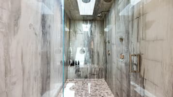 A modern bathroom with a glass shower enclosure, marble walls, and a tiled floor.