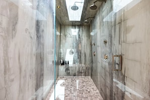 Un baño moderno con cabina de ducha de vidrio, paredes de mármol y suelo de baldosas.