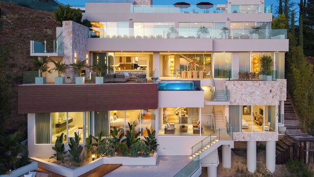 Una casa moderna de varios pisos con un balcón grande, una piscina y una escalera que lleva a los niveles superiores.