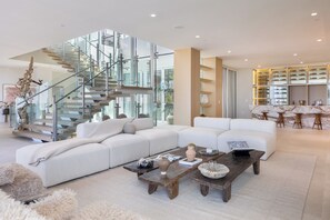 Una sala de estar moderna con un sofá seccional blanco, una mesa de centro de madera y una escalera de cristal.
