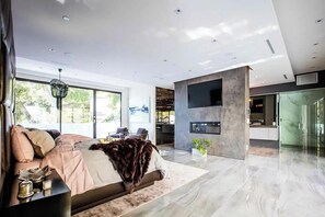 Ein modernes Interieur mit einem großen Bett, einem an der Wand befestigten Fernseher und einer Glastür zum Badezimmer.