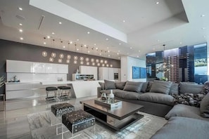 Ein modernes Wohnzimmer mit einer Couch, Hocker, einem Couchtisch und einer Küche im Hintergrund.