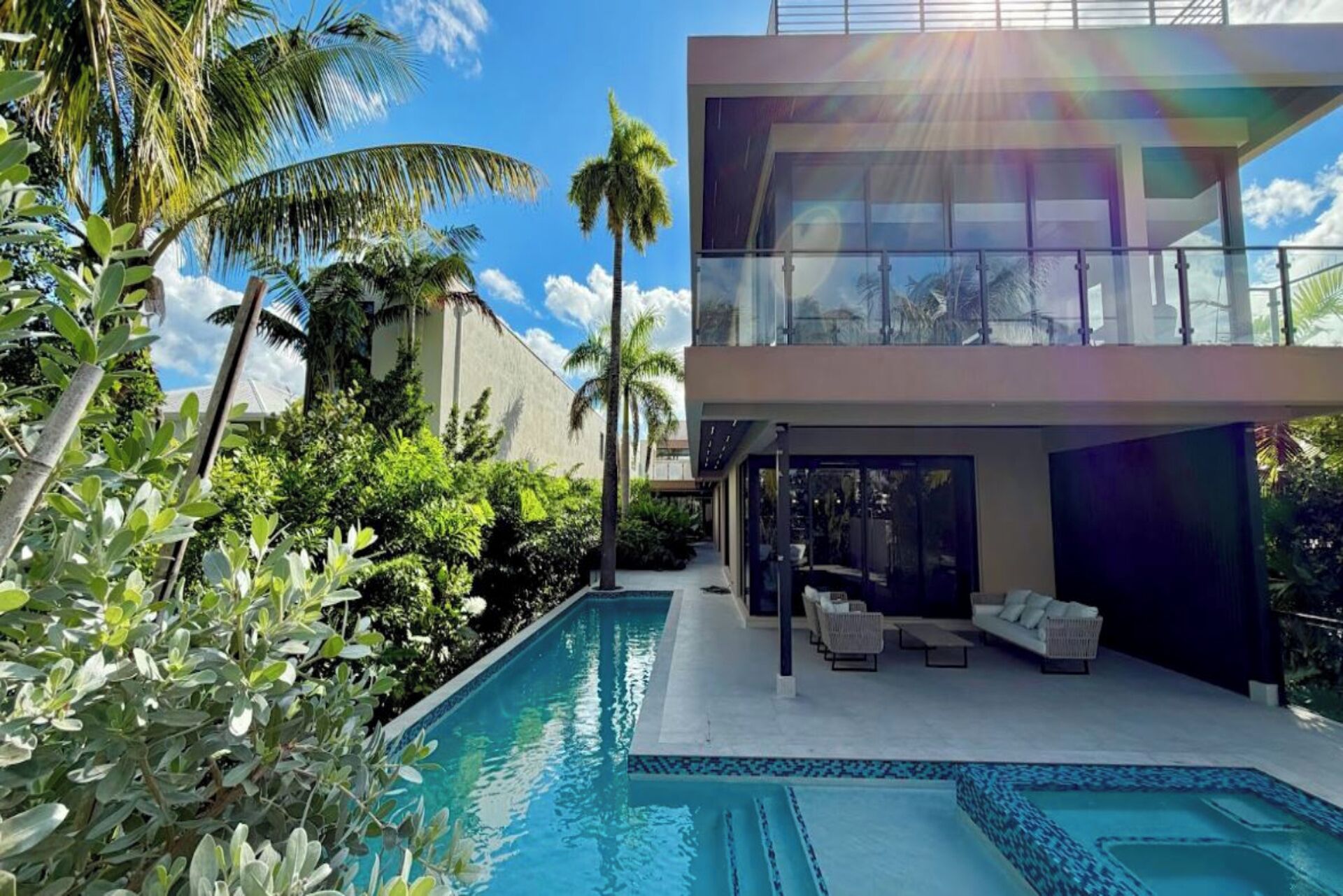 A modern two-story house with a swimming pool, outdoor seating, and lush greenery.