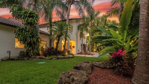 A modern house with a well-maintained garden, including palm trees and a lawn. - Perla (Miami Shores)