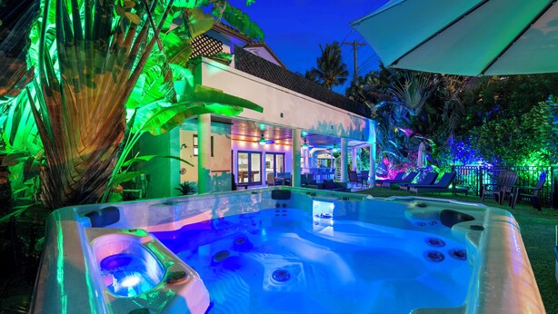 A hot tub with a poolside area, surrounded by tropical plants and a building with a tiled roof. - Perla (Miami Shores)