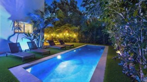 Une piscine avec des chaises longues, une pelouse bien entretenue et un bâtiment doté d’une fenêtre.