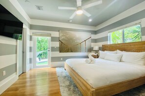 A bedroom with a wooden bed, a ceiling fan, a large window with a view of greenery, and a door leading to an outdoor area. - Villa Carrera (Miami)