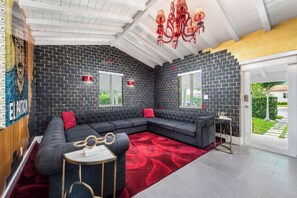 A modern living room with a dark brick wall, a sectional sofa, a red rug, and a chandelier.