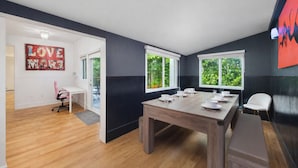 Un coin repas avec une table en bois dressée pour quatre personnes, un banc et une vue sur la verdure à travers les fenêtres.