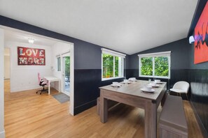 Un coin repas avec une table en bois dressĂ©e pour quatre personnes, un banc et une vue sur la verdure Ă travers les fenĂȘtres.