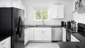 Une cuisine moderne avec des meubles blancs, un réfrigérateur noir, une fenêtre donnant sur un espace verdoyant et un plan de travail noir.
