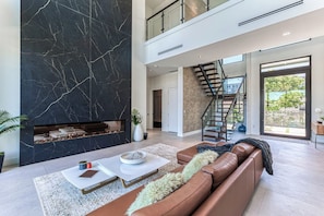 Ein modernes Wohnzimmer mit Kamin, einer Treppe und Blick ins Freie.