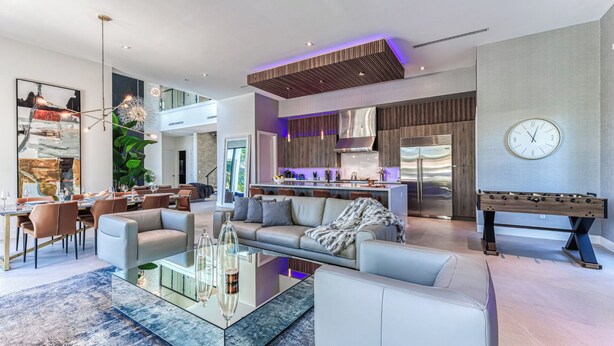 A modern living room with a glass coffee table, sofas, and a kitchen area with a foosball table. - Brielle (Fort Lauderdale)