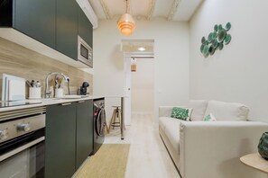 Eine moderne Küche mit Einbauofen, Mikrowelle und Kaffeemaschine. Im Wohnbereich befindet sich ein weißes Sofa mit grünen Kissen.