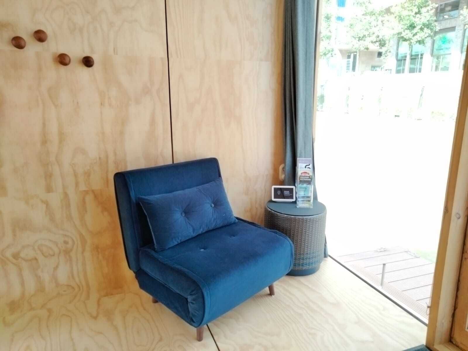 Ein blaues Sofa mit Kissen, ein kleiner runder Tisch mit einem Ger ät und eine Holzwand mit einer vertikalen Platte.