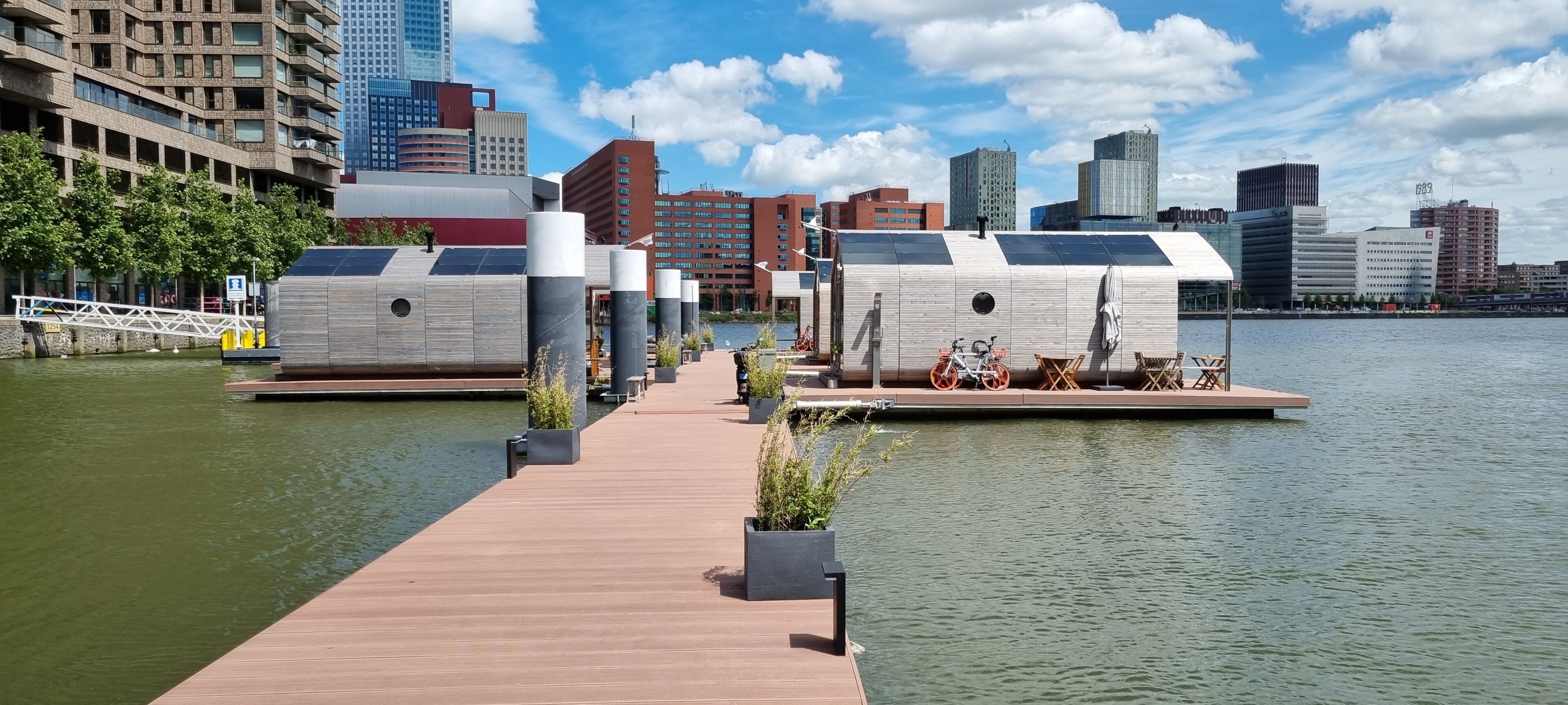 A waterfront property with a wooden dock, floating structures, and a cityscape in the background.