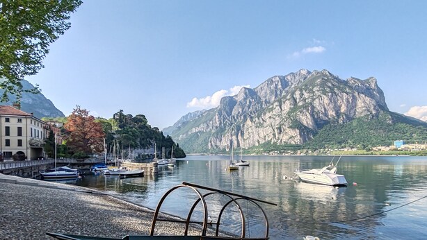 A boat named 'MALGRATE' on a pebbled shore with a lake, boats, and mountains in the background. - Cozy 2-bedroom apartment in enchanting Malgrate with AC (Malgrate)