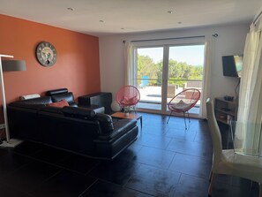 Ein modernes Wohnzimmer mit einem schwarzen Ledersofa, einem roten Sessel, einem Glastisch und einem großen Fenster mit Blick ins Freie.