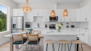 Una cucina moderna con mobili bianchi, un'isola centrale, sgabelli da bar e illuminazione a sospensione.