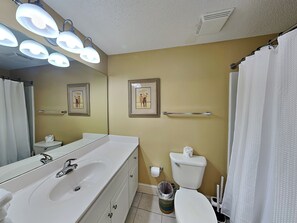 Une salle de bain avec un lavabo blanc, un miroir et des toilettes, un rideau de douche et deux tableaux encadrés au mur.