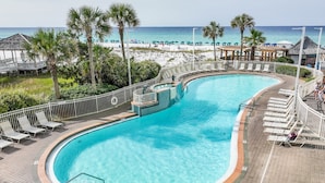 A pool with a curved design, surrounded by lounge chairs and a deck. - Pelican Beach #2004 | Gulf Front in Destin + Amenities (Destin)