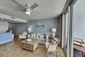 A modern living room with a ceiling fan, a sofa set, a coffee table, and a view through large windows. - Pelican Beach #2004 | Gulf Front in Destin + Amenities (Destin)