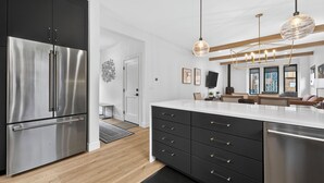 Une cuisine moderne dotée d’un réfrigérateur en acier inoxydable, de meubles de cuisine noirs et d’un plan de travail blanc.