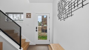 Un intérieur moderne avec un escalier, un banc en bois, une porte donnant sur une vue agréable et un luminaire fixé au mur.