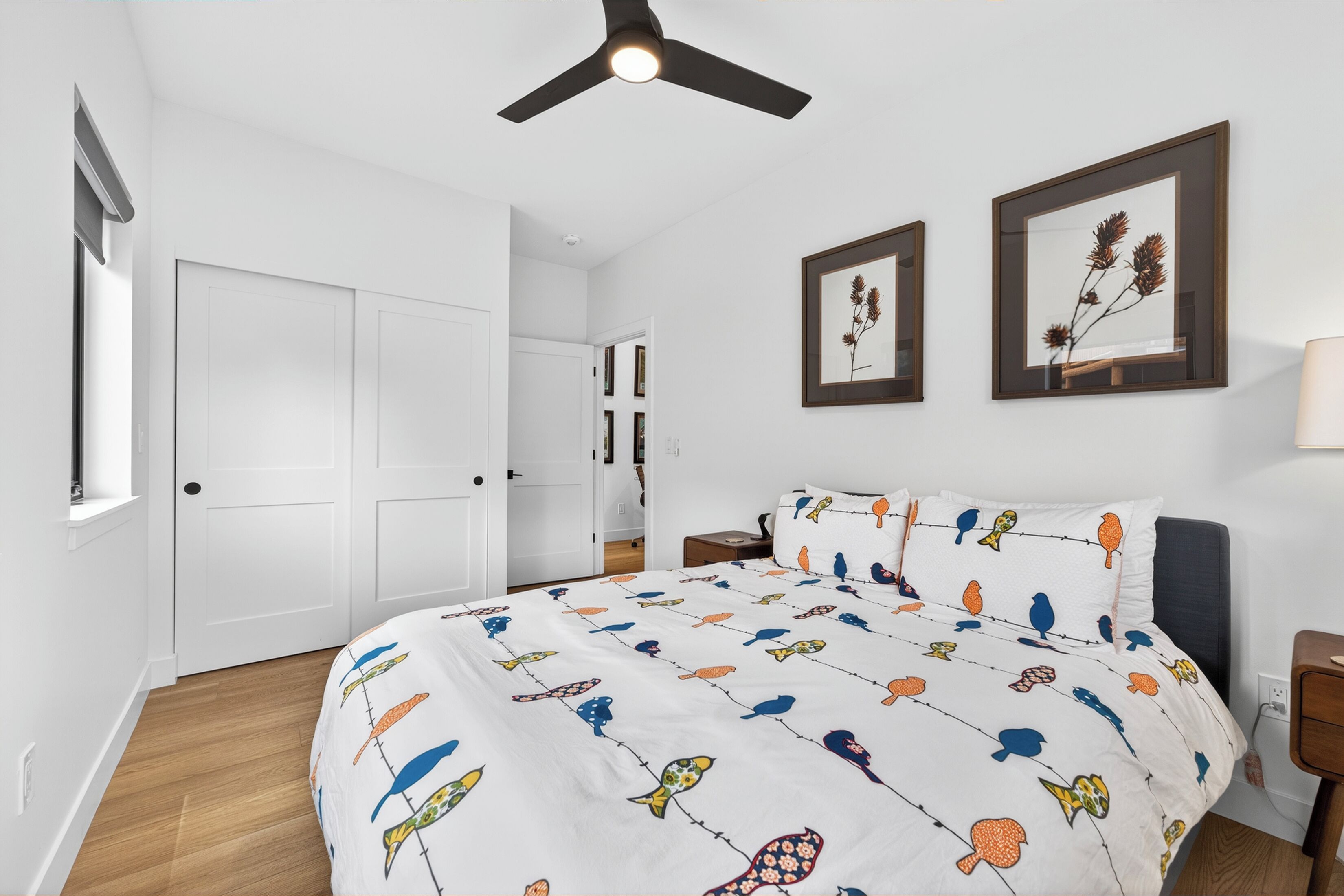 Une chambre à coucher avec un lit, un ventilateur de plafond, des tableaux encadrés accrochés au mur et une fenêtre.