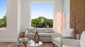 Uma sala de estar moderna com uma janela grande, uma mesa de centro de vidro e um sofá.
