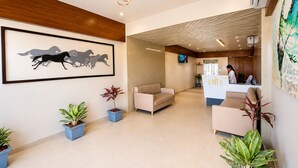 A reception area with a reception desk, seating, potted plants, a framed artwork of horses, and a modern ceiling light fixture. -  Hotel Akshar Imperial Morbi (Morbi)