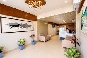 A reception area with a reception desk, seating, potted plants, a framed artwork of horses, and a modern ceiling light fixture. -  Hotel Akshar Imperial Morbi (Morbi)