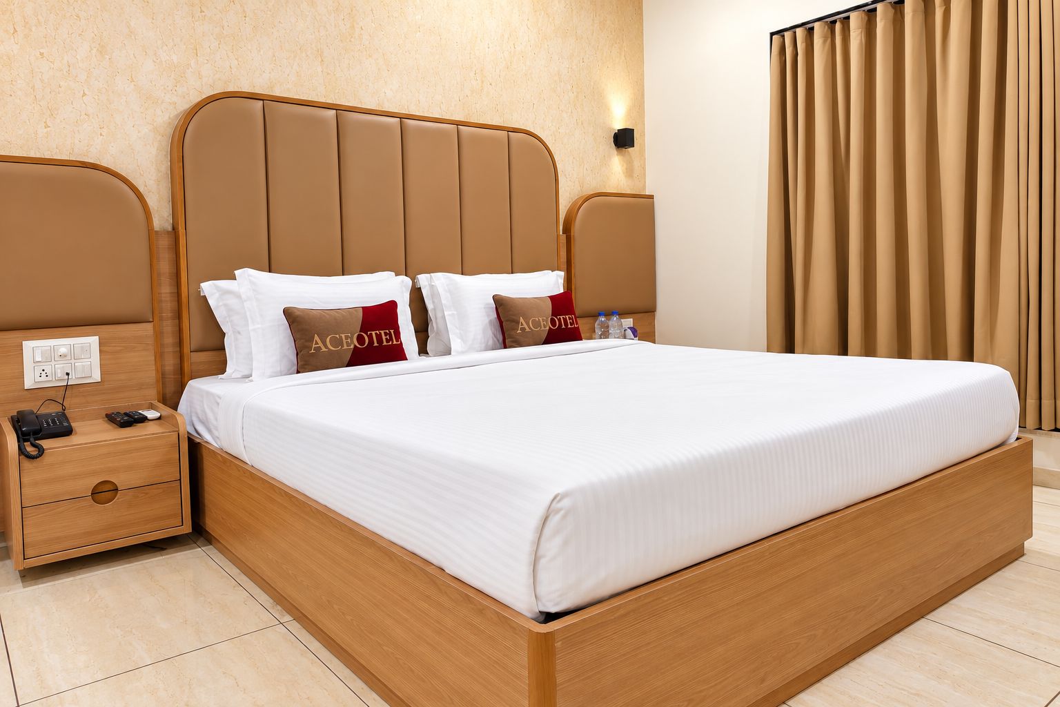 A hotel room with a large bed, wooden headboard, two bedside tables, a nightstand, and a wall-mounted light.
