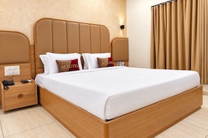 Habitación de hotel con una cama grande, cabecera de madera, dos mesitas de noche y una lámpara de pared.