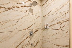 Baño con pared de mármol, cabezal de ducha y dispensador de jabón.