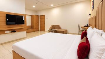 Habitación de hotel con una cama grande, televisión montada en la pared, armario de madera, una mesita y una silla.