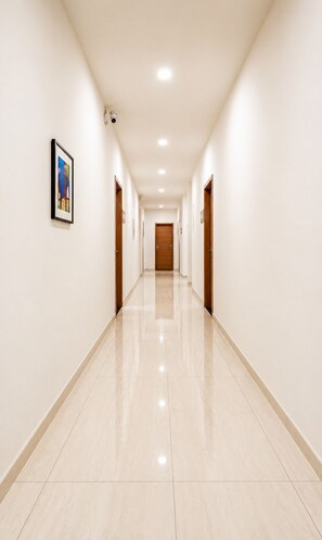A long, narrow hallway with a polished floor, doors on both sides, and recessed lighting. -  Hotel Akshar Imperial Morbi (Morbi)