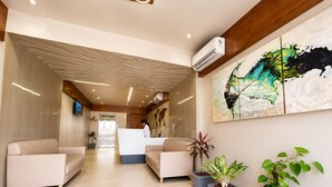 A reception area with a counter, two sofas, and potted plants. -  Hotel Akshar Imperial Morbi (Morbi)